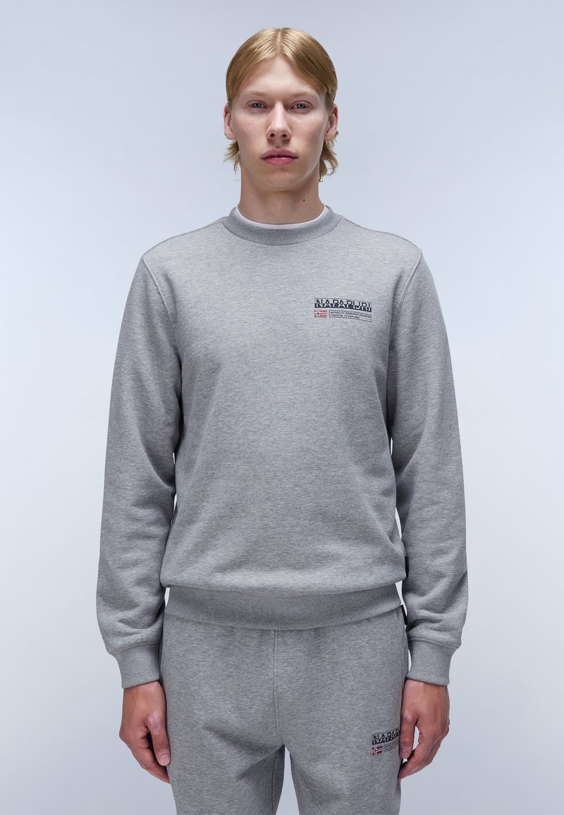 Sudadera gris de material suave, con cuello redondo, puños de canalé y un parche de logo en el lado izquierdo del pecho.
