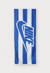 Toalha listrada em azul e branco com um grande logótipo da Nike em branco com contornos azuis. Feita de um tecido macio e absorvente.