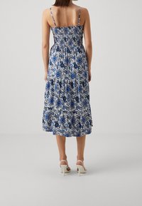 Maxi šaty s modrým květinovým vzorem na bílém pozadí, s nařaseným korzetem a nastavitelnými ramínky, zakončené volánkovým lemem.