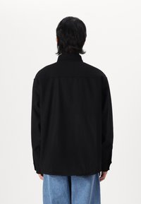 Zwarte langemouwen shirt met een kraag, met een relaxte pasvorm en zijhemsplitsingen. Draagt met lichtblauwe wijdvallende jeans.