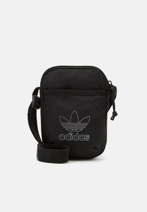 Must mustriba mustkott, millel on lukuga sulgemine, valge Adidas kolmnurga logo ja reguleeritav rihm. Ristkülikukujuline kuju, sile tekstuur.