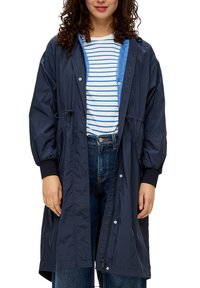 Granatowa, lekka kurtka z troczkami w pasie, zatrzaskami i elastycznymi mankietami; noszona na niebiesko-białą koszulę w paski.