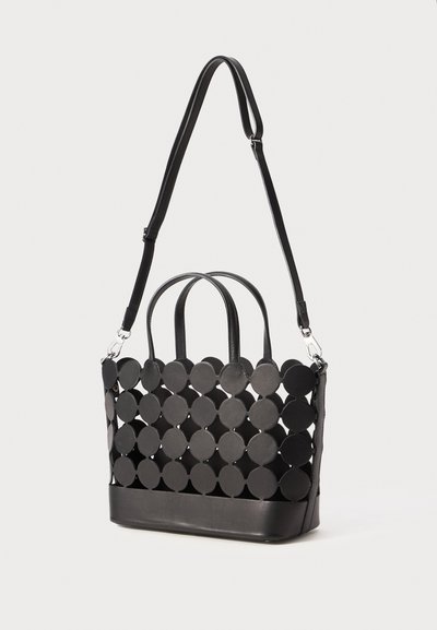Sac à main noir avec des découpes circulaires, doté de deux poignées et d'une bandoulière amovible. Fabriqué en cuir, base rectangulaire structurée.