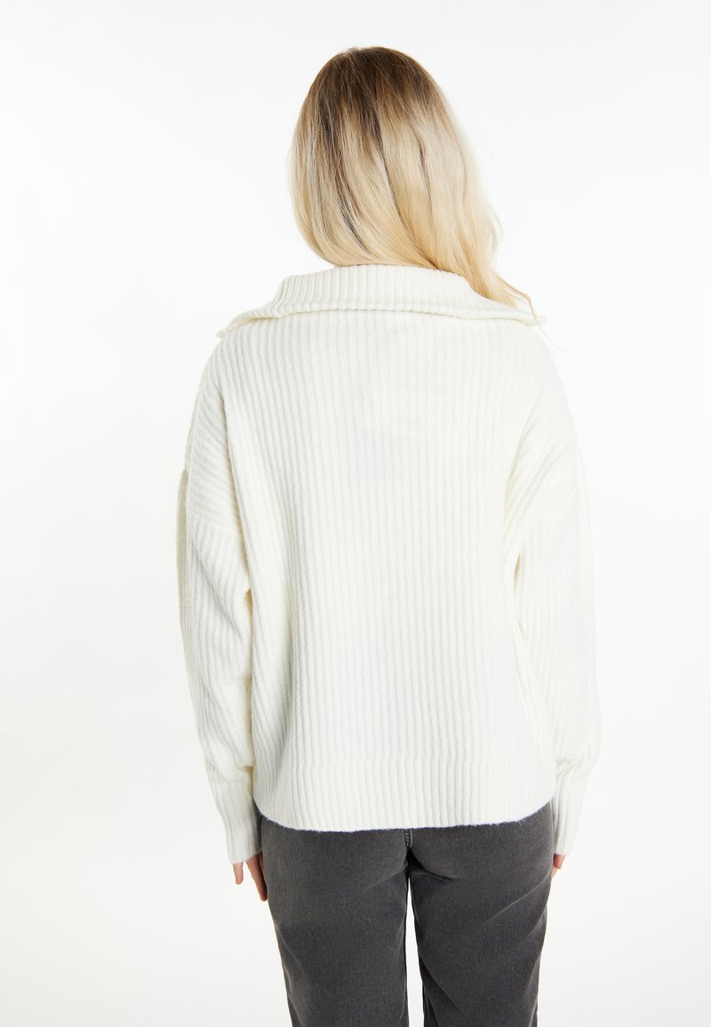 Weißer gerippter Pullover mit Rollkragen und übergroßem Schnitt, kombiniert mit dunkelgrauen Hosen. Verfügt über lange Ärmel und einen cropped Saum.