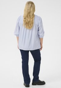 Blusa a righe blu chiaro con maniche a sbuffo, vestibilità rilassata e orlo curvo, abbinata a jeans scuri e calzature nere.