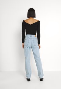 Top nero a coste senza spalle abbinato a jeans high-waisted di colore azzurro chiaro. I jeans presentano un classico design a cinque tasche e una patch in pelle.