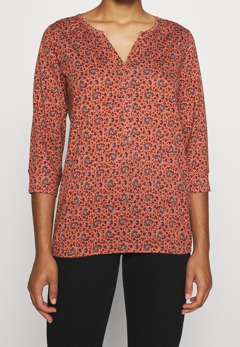 Top a maniche lunghe in ruggine con stampa paisley. Presenta una scollatura a V e chiusura con bottoni. Realizzato in un tessuto leggero e testurizzato.