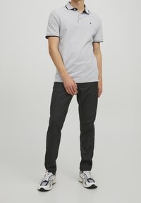 Grå kortärmad polo med svarta detaljer på kragen och ärmarna, kombinerad med mörka smalna byxor och sneakers.