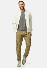 Letvægts cremet bomberjakke over en grå tekstureret sweater, parret med khaki cargo-bukser med flere lommer og elastiske manchetter.