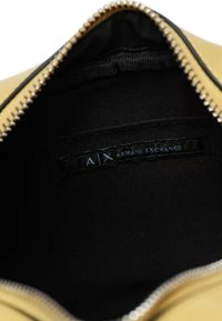 Interno giallo di una borsa con una fodera nera, dotata di una cerniera argentata. Un'etichetta mostra il testo "A|X ARMANI EXCHANGE" in nero.