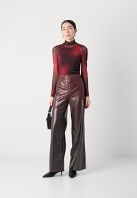 Doorzichtig longsleeve top in bordeauxrood met een aansluitend lijfje; hoogelastiche bruine nep leren wide-leg broek; scherpe zwarte hakken; kleine zwarte handtas.