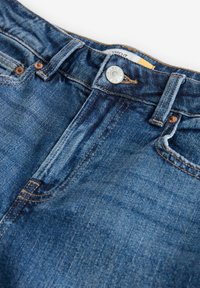 Modré džíny z denimu s středním pasem, zapínáním na knoflík a měděnými nýty. Mají jemné zesvětlení a rovný střih nohavic.