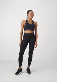 Soutien-gorge de sport noir avec un décolleté en forme de scoop, associé à un legging noir taille haute. L'ensemble présente une texture lisse et un design ajusté.