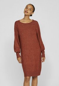 Abito maglione in colore ruggine con una vestibilità ampia, scollatura larga a barca e maniche a palloncino. Tessuto texture con polsini e orlo a coste.