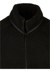Giacca in pile nera con colletto alto, dotata di zipper a tutta lunghezza. Il tessuto ha un aspetto texturizzato e soffice, ed è leggero.