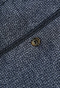 Strukturierten marineblauen Stoff mit einem dezenten Muster, ergänzt durch einen braunen Vierlochknopf und dunkle Fadendetails entlang des Randes.