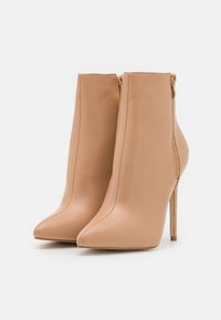 Nudefarbene Leder-Ankle Boots mit spitzem Zehenbereich, seitlichem Reißverschluss und Stiletto-Absatz. Glatte Textur und saubere Nahtdetails.