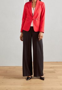 Rød blazer med en indsnævret talje og sølvhardware, parret med sorte brede bukser og spidse sorte hæle.