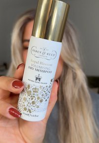 Vit aerosolburk med guldlock, märkt "Royal Blossom Volymerande Torrschampo", med blommiga guldaccenter och en kapacitet på 50 ml.