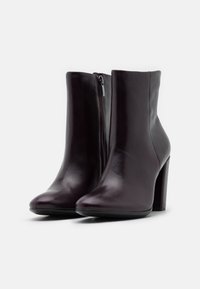 Stivali ankle in pelle borgogna con finitura liscia, tacco a blocco alto e zip laterale per la chiusura. Punta rotonda e silhouette elegante.