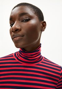 Rot- und marinegestreifter Rollkragenpullover aus weichem Stoff. Verfügt über einen enganliegenden Kragen und ein schlankes Design.