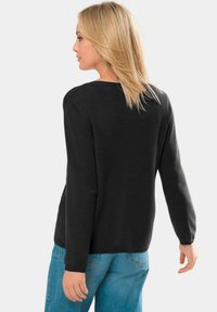 Dunkelgrauer Strickpullover mit langen Ärmeln, rundem Halsausschnitt und lockerer Passform, kombiniert mit hellblauen Denim-Jeans. Weiche Textur.