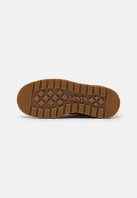Semelle de chaussure marron avec des crampons profonds et des motifs en forme de losange, avec le logo « Levi's » embossé au centre.