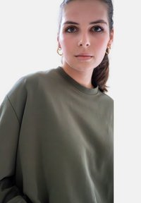 Olijfgroene oversized sweatshirt met een gladde textuur en een ronde halslijn, weergegeven tegen een lichte achtergrond.