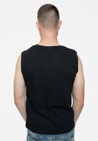 Black sleeveless cotton tank top with a round neck, shown from the back, paired with light blue denim jeans. Simple design, no patterns.