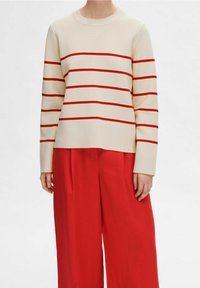 Cremfarbener Pullover mit roten horizontalen Streifen, runder Ausschnitt und langen Ärmeln, kombiniert mit lockeren roten Hosen. Strukturierter Strickstoff.