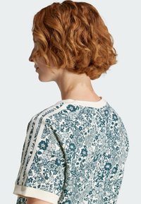 T-shirt a maniche corte con un motivo floreale verde e bianco, colletto a costine color crema e dettagli a righe sulle spalle.