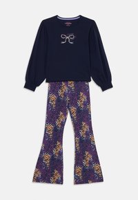 Haut à manches longues bleu marine avec un motif de nœud et pantalon violet évasé orné d'un motif animalier orange et jaune.