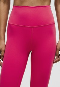 Hooggetailleerde roze legging gemaakt van rekbare stof met een gladde textuur, voorzien van platte naden en een aansluitend ontwerp.