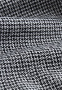 Mustvalge houndstooth-kanga lähivaade, millel on tekstuuriga kudumismuster ja kerge voldi tõttu varjud ja sügavus.