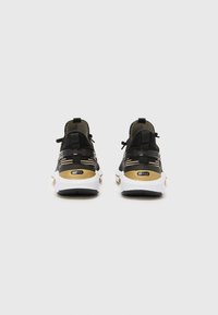 Chaussures de sport noires et dorées avec dessus en mesh, talon rembourré, semelles blanches et semelles extérieures texturées noires. Bandes réfléchissantes sur les côtés.