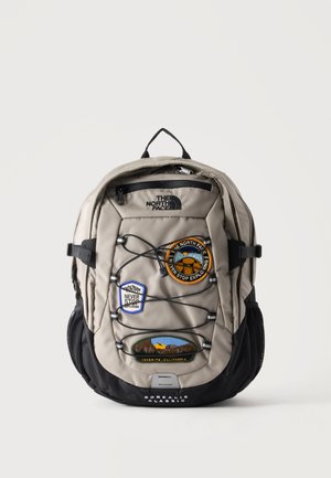 Szaro-czarny plecak North Face Borealis Classic z trzema kolorowymi naszywkami o tematyce wędrówek i przednim elastycznym sznurkiem bungee.