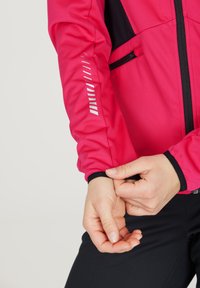 Fuchsia jacket with black accents, featuring a zip closure, elastic cuffs, and reflective strip details on the sleeves. Textured, smooth fabric.