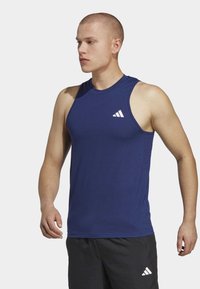 Sötétkék, ujjatlan sportpóló sima anyagból, a bal mellen fehér Adidas logóval. Kényelmes nyakkivágással.