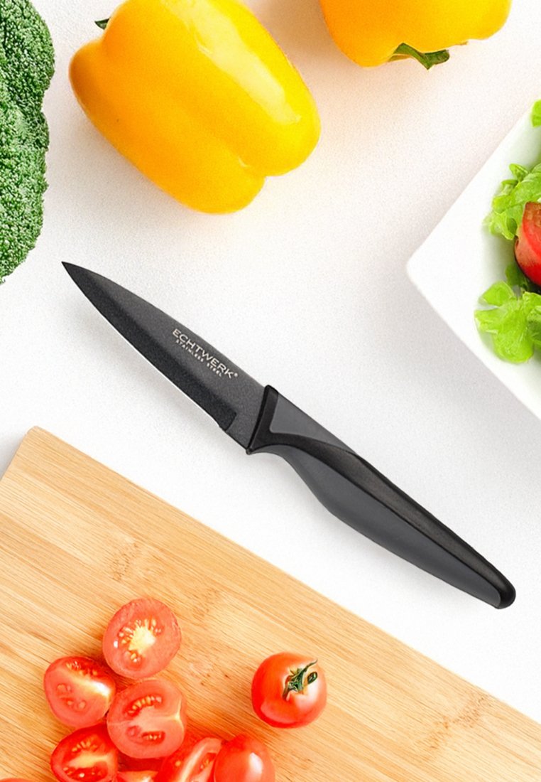 Couteau d'office noir avec un manche lisse, doté d'une lame aiguisée. Entouré d'un poivron jaune, de brocoli et de tomates cerises sur une planche à découper.