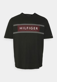 Musta lyhythihainen T-paita, joka on valmistettu puuvillasta. Paitassa on vaakasuora punavalkoinen raitapaneeli, jonka keskellä on "HILFIGER"-logo.