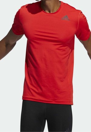 Persona que lleva una camiseta deportiva Adidas de manga corta de color rojo brillante y mallas negras, mostrada desde el cuello hasta la parte superior de los muslos.