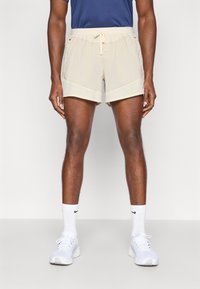 Ανοιχτό μπεζ αθλητικά σορτς με ελαστική μέση και κορδόνι, που διαθέτουν πλαϊνές τσέπες και αεριζόμενο πλέγμα στο τελείωμα.