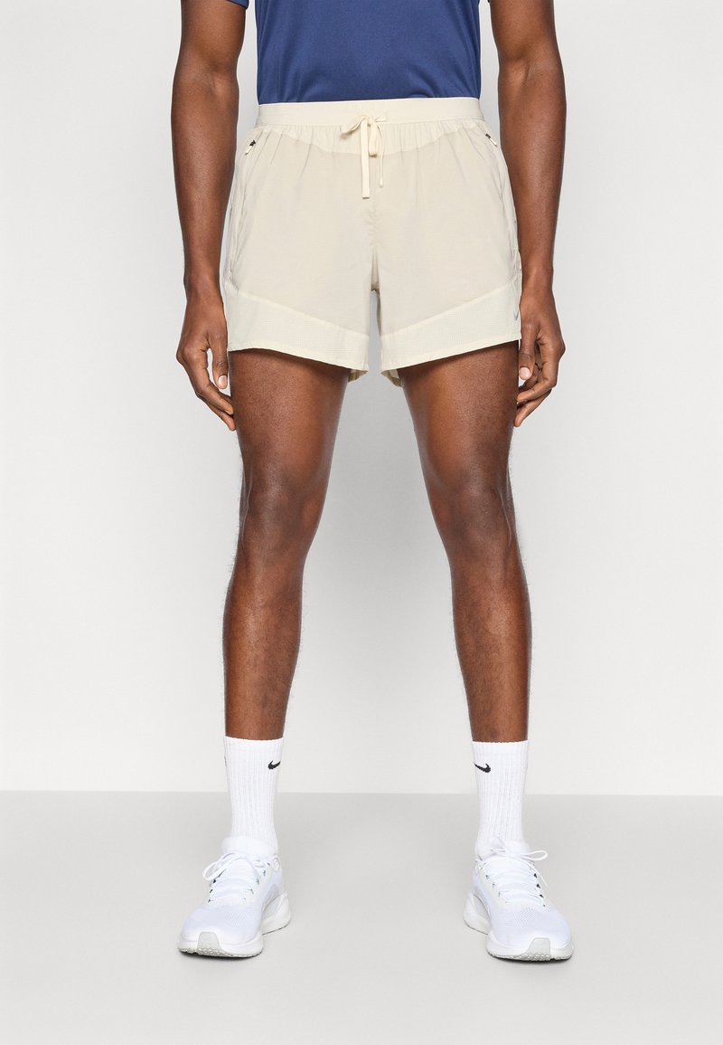 Ανοιχτό μπεζ αθλητικά σορτς με ελαστική μέση και κορδόνι, που διαθέτουν πλαϊνές τσέπες και αεριζόμενο πλέγμα στο τελείωμα.