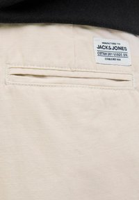 Béžová bavlněná tkanina s hladkým povrchem, obsahující zadní kapsu a štítek s nápisem "Jack & Jones Cotton Dry Goods Div."