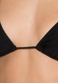 Schwarzer Bikini-Oberteil mit einem Dreiecksdesign, dünnen Trägern, gerafftem Material und minimalem Zubehör an den Seiten.