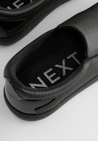 Pantofi negri tip slip-on, cu un superior din piele texturată și talpă din cauciuc neted. Prezentând o căptușeală din țesătură și un logo vizibil al brandului în argint.