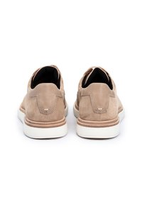 Scarpe in suede beige con una superficie liscia, dotate di una suola in gomma bianca a contrasto e un design arrotondato. La vista posteriore mette in evidenza un décor di cuciture uniche.