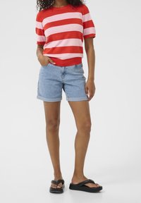 Red and pink striped knit top with short sleeves, paired with denim shorts. Model wears black platform sandals. Smooth texture, casual design.