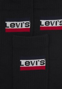Schwarze Socken aus Strickstoff mit einem Levi's-Logo in weißen, roten und blauen horizontalen Streifen am oberen Rand.