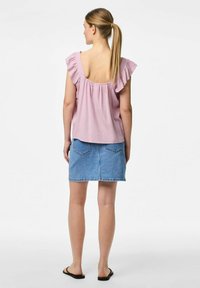 Top rosa con rouches e apertura sul retro, abbinato a una mini gonna di jeans blu con due tasche posteriori, e infradito nere.
